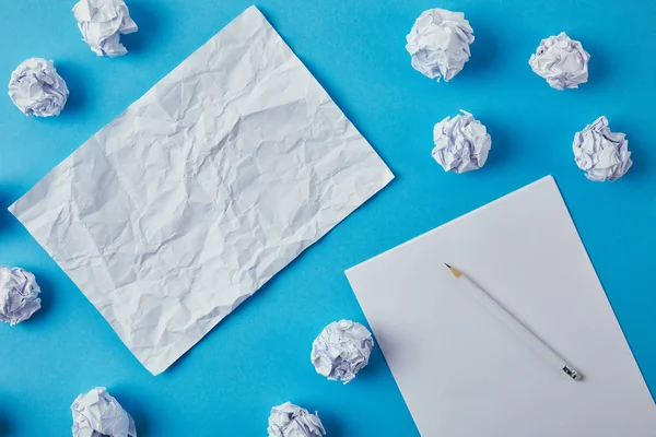 Top view of crumpled papers with blank papers and pencil on blue tabletop — Stock Photo