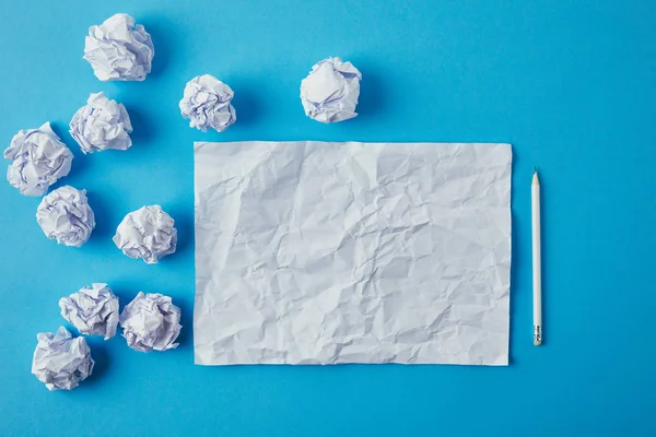 Top view of crumpled papers and pencil on blue surface — Stock Photo