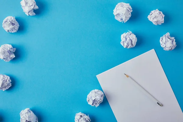 Top view of crumpled papers with blank paper and pencil on blue surface — Stock Photo