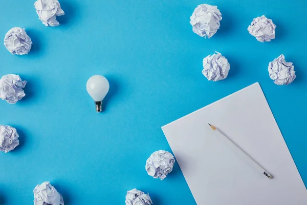 Top view of power saving light bulb with crumpled papers on blue surface — Stock Photo