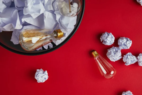 Vue du dessus de la poubelle de bureau avec des papiers froissés et des lampes à incandescence vintage sur le dessus de table rouge — Photo de stock