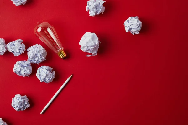 Top view of crumpled papers with light bulb and pencil on red surface — Stock Photo