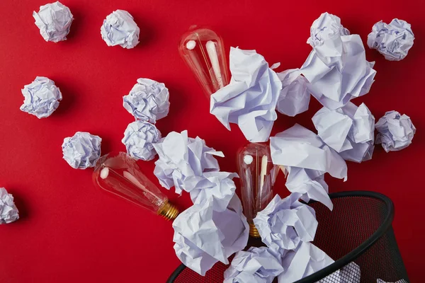 Top view of crumpled papers with vintage incandescent lamps spilled from trash bin on red tabletop — Stock Photo