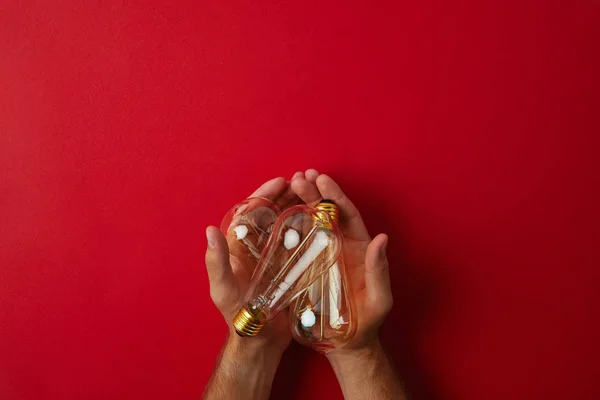 Tiro recortado del hombre sosteniendo lámparas incandescentes vintage en la mesa roja - foto de stock