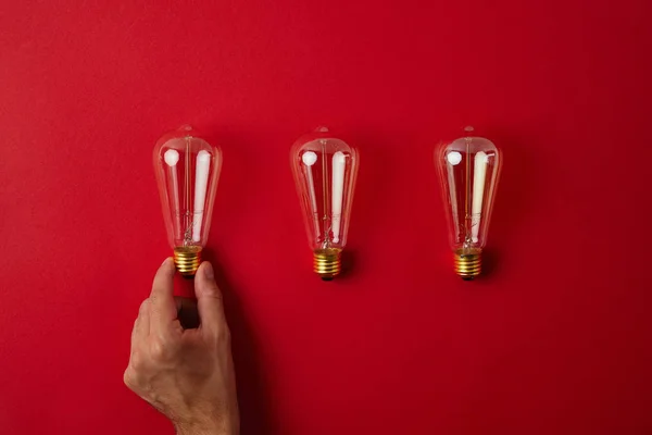 Abgeschnittene Aufnahme eines Mannes, der Vintage-Glühlampen hintereinander auf roter Tischplatte arrangiert — Stockfoto