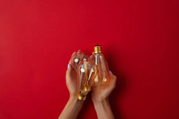 Tiro recortado de mujer sosteniendo lámparas incandescentes vintage en la mesa roja - foto de stock