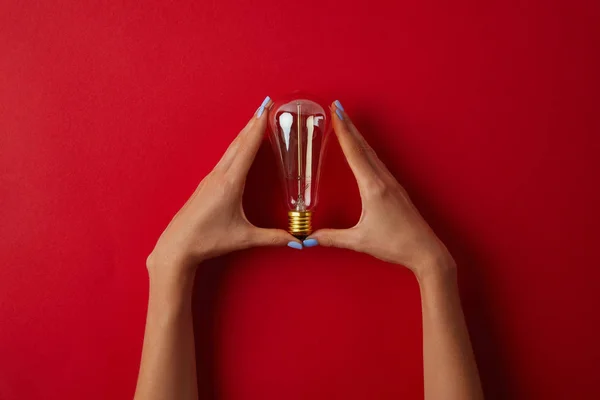 Plan recadré de femme tenant lampe à incandescence vintage sur le dessus de table rouge — Photo de stock