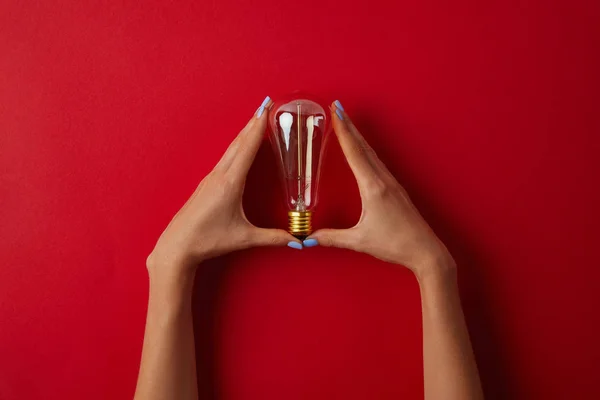 Tiro cortado de mulher segurando lâmpada incandescente vintage na mesa vermelha — Fotografia de Stock