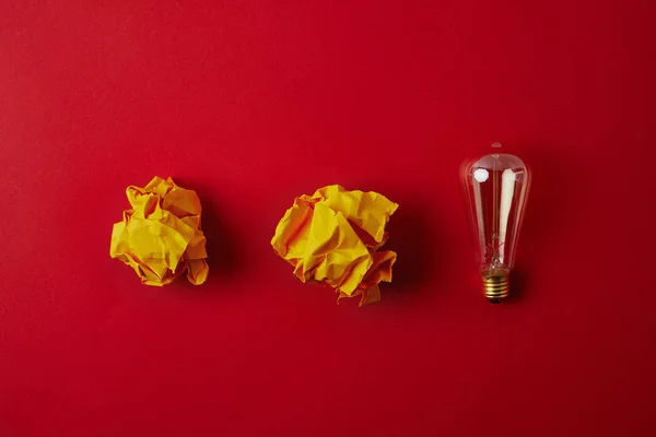 Vista superior de papeles amarillos arrugados con lámpara incandescente sobre superficie roja - foto de stock