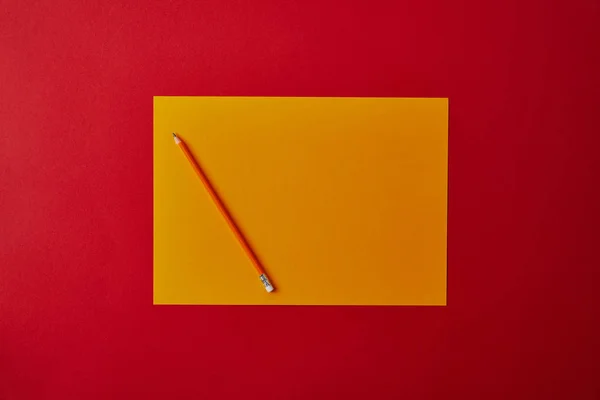 Vue du dessus du papier jaune vierge avec crayon sur la surface rouge — Photo de stock