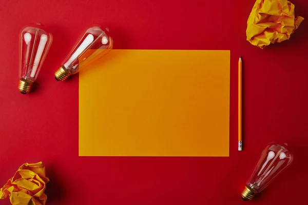 Vista superior de papel blanco amarillo con papeles arrugados y lámparas incandescentes sobre superficie roja - foto de stock