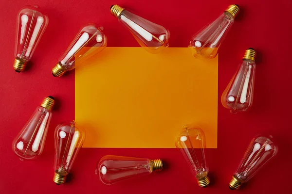 Vue de dessus des lampes à incandescence vintage sur la surface rouge avec du papier blanc jaune — Photo de stock