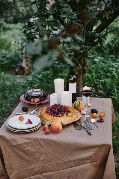 Gustosa torta di frutti di bosco appetitosa, vino e candele sul tavolo in giardino — Foto stock