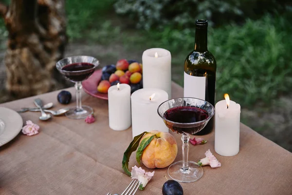 Velas y vino tinto en la mesa en el jardín - foto de stock