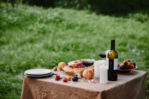 Свічки, пляшка вина та фрукти на столі в саду — Stock Photo