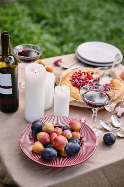 Frutas, velas y botella de vino en la mesa en el jardín - foto de stock