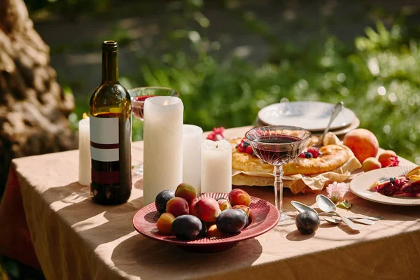 Kerzen, Wein und leckere Früchte auf dem Tisch im Garten — Stockfoto