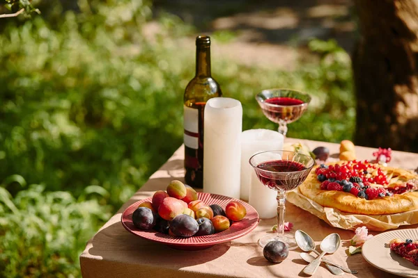 Velas, gafas de vino y frutas en la mesa en el jardín - foto de stock