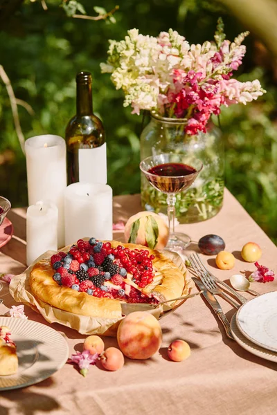 Candles, wine and berries pie on table in garden — Stock Photo