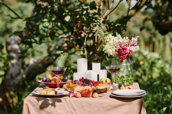 Velas, vino y frutas en la mesa en el jardín - foto de stock