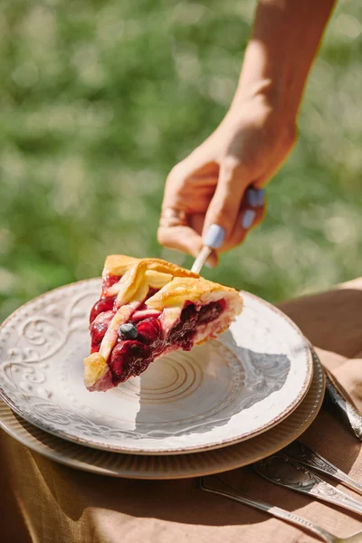 Abgeschnittenes Bild einer Frau, die im Garten ein Stück Kuchen auf den Teller legt — Stockfoto