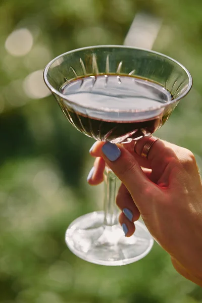 Imagen recortada de mujer sosteniendo vidrio con vino tinto sobre hierba verde - foto de stock