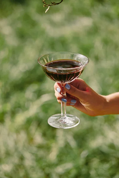 Cropped image of woman holding transparent wineglass above green grass — Stock Photo