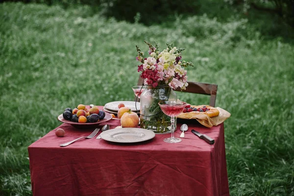 Wineglass, tasty berries pie and bouquet of flowers on table in green garden — Stock Photo