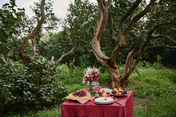 Torta de bagas e buquê de flores na mesa no jardim com árvores — Fotografia de Stock