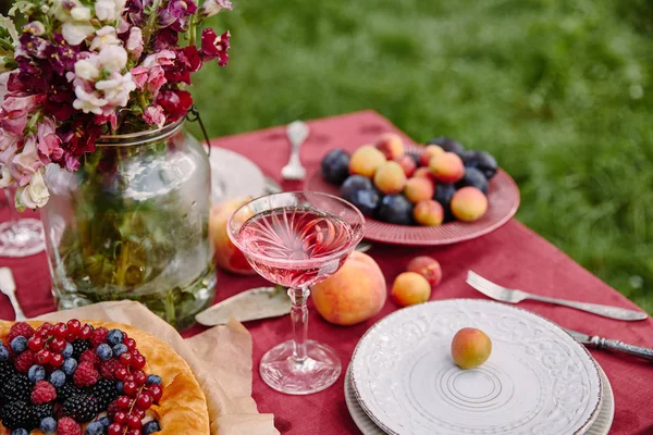 Ягодный пирог, бокал вина и букет цветов на столе в саду — стоковое фото