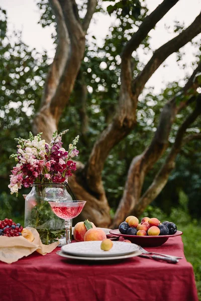 Bouquet di fiori, frutta e bicchieri da vino sul tavolo in giardino — Foto stock