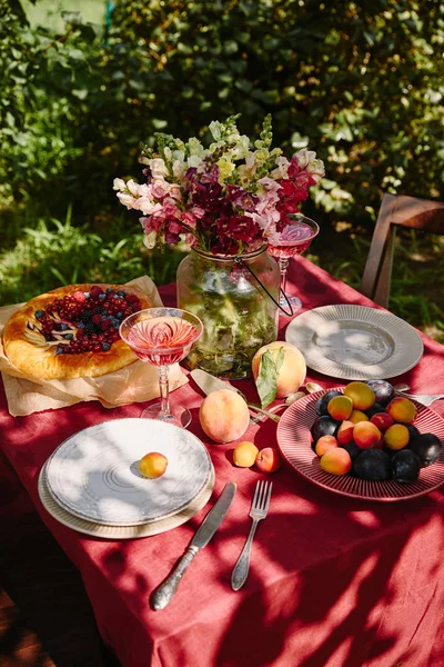 Букет квітів, фруктів і апетитного пирога на столі в саду — стокове фото