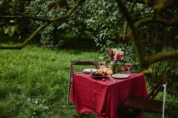 Blumenstrauß, Weingläser und Früchte auf dem Tisch im Garten — Stockfoto