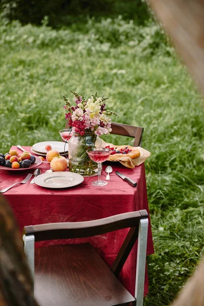 Букет квітів у скляній банці і фрукти на столі в саду — Stock Photo