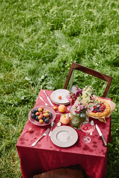 Vista de ángulo alto de la mesa con frutas, tarta y flores en el jardín - foto de stock