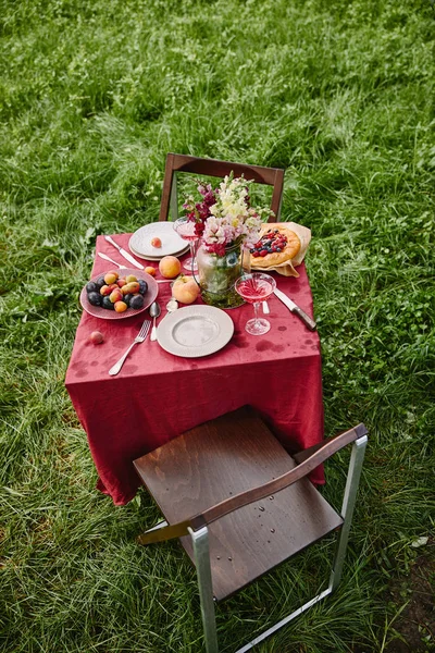 Vista de ángulo alto de la mesa con frutas, tarta y platos en el jardín - foto de stock