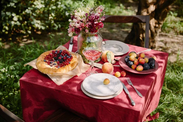 Copa de vino, tarta de bayas y frutas en la mesa en el jardín - foto de stock