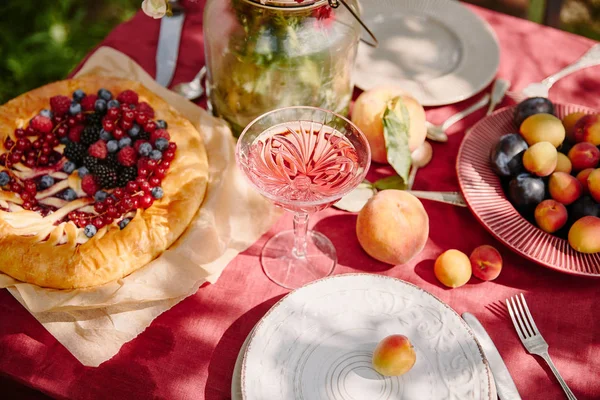 Copa de vino, tarta de bayas y frutas en la mesa en el jardín con luz solar - foto de stock