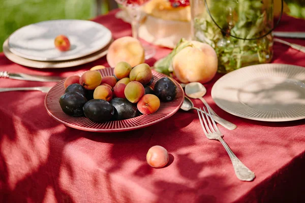 Früchte, Gabeln und Teller auf dem Tisch im Garten — Stockfoto