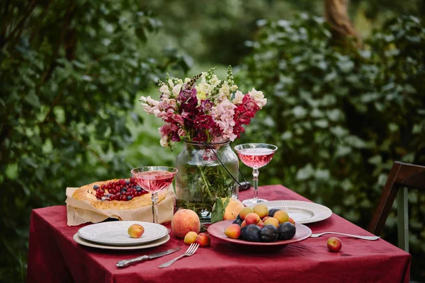 Ramo de flores en frasco de vidrio y gafas de vino en la mesa en el jardín - foto de stock