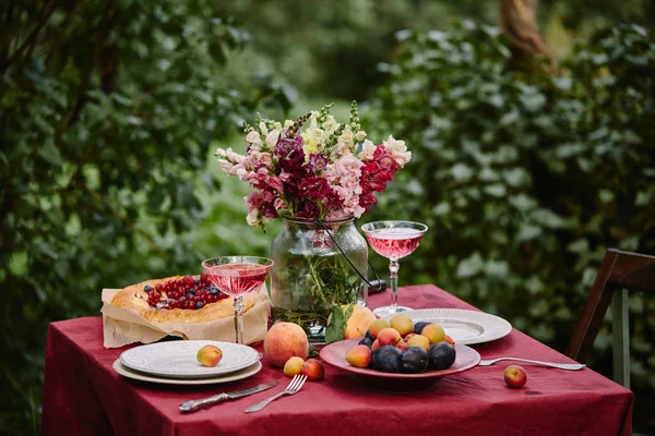 Bouquet of flowers in glass jar and wineglasses on table in garden — Stock Photo