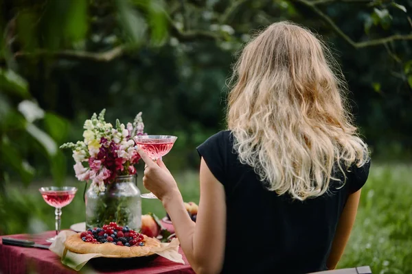 Vue arrière de la femme tenant un verre de vin à table dans le jardin — Photo de stock