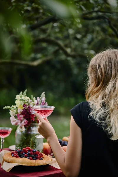 Back view of woman holding glass of wine at table in garden — Stock Photo