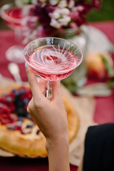 Обрізане зображення жінки, що тримає келих рожевого вина за столом в саду — стокове фото