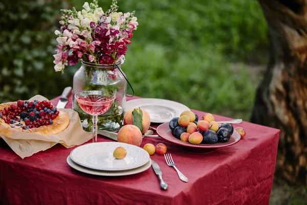 Vasos de vino, tarta de bayas y frutas en la mesa en el jardín - foto de stock