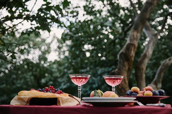 Glasses of wine, berries pie and fruits on table for dinner in garden — Stock Photo