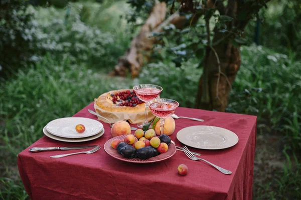 Copos de vinho, torta de bagas, pratos e frutas na mesa no jardim — Fotografia de Stock