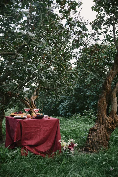 Mesa servida con mantel rojo en el jardín - foto de stock