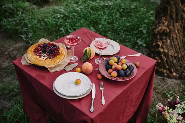 Vista de ángulo alto de tarta de bayas y copas de vino en la mesa en el jardín - foto de stock