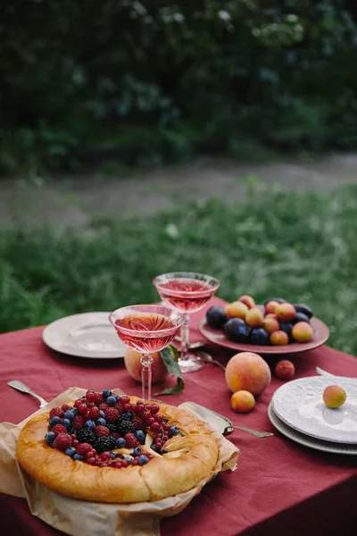 Appetizing berries pie and glasses of wine on table in garden — Stock Photo